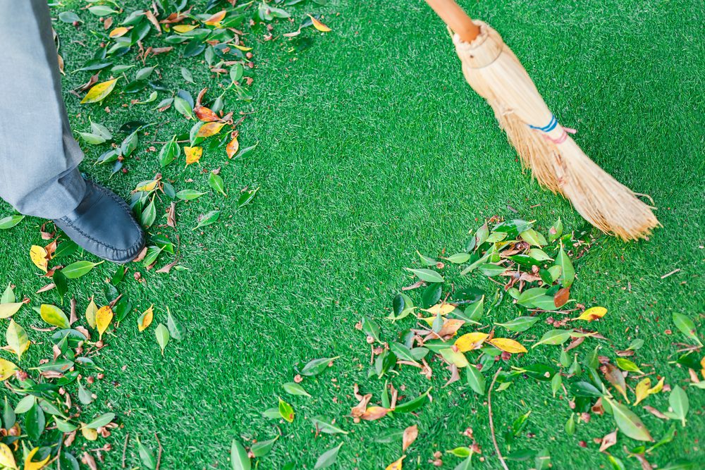 Person sweeping leaves off artificial grass with a broom.