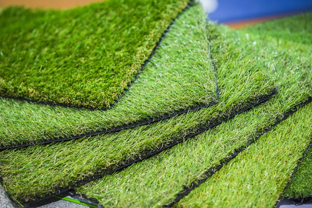 Stack of artificial grass samples in various shades of green for landscaping.