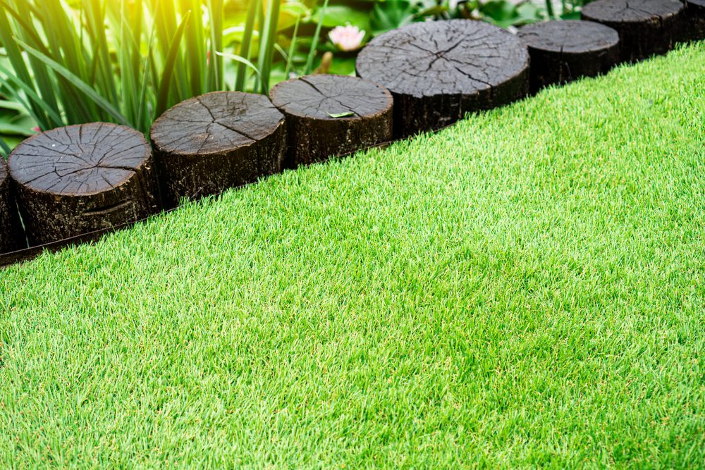 Artificial grass lawn bordered by rustic wooden logs in a garden setting.